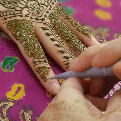 A henna cone adding the final touches to the fingertip of a larger hand henna design