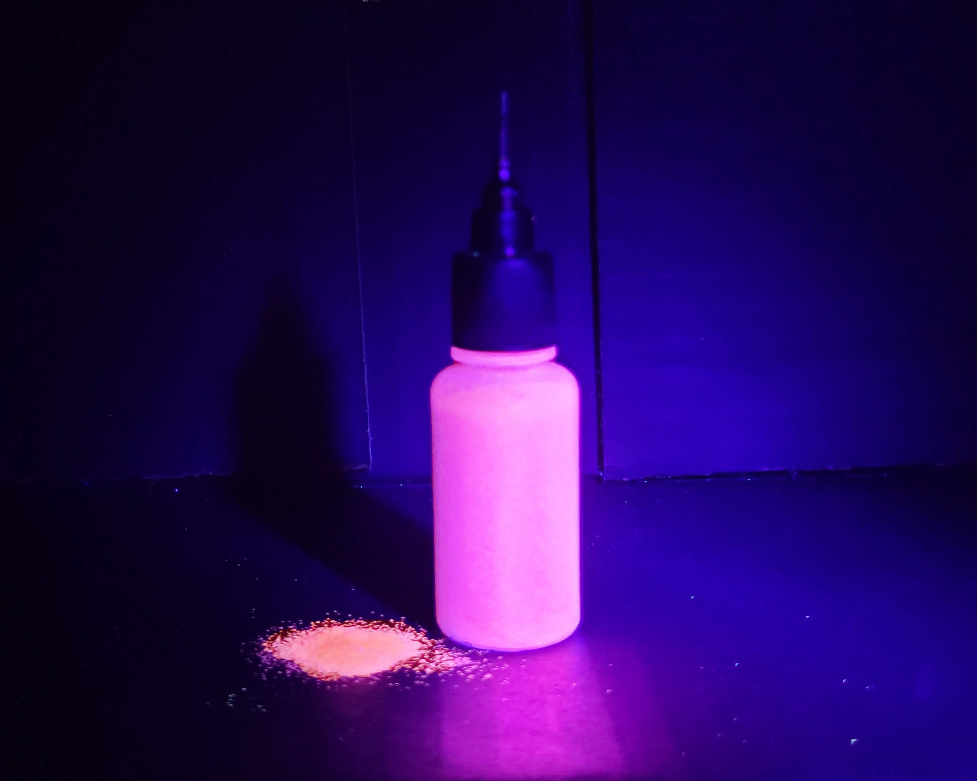 bottle of UV glitter with UV light- glowing pink/orange