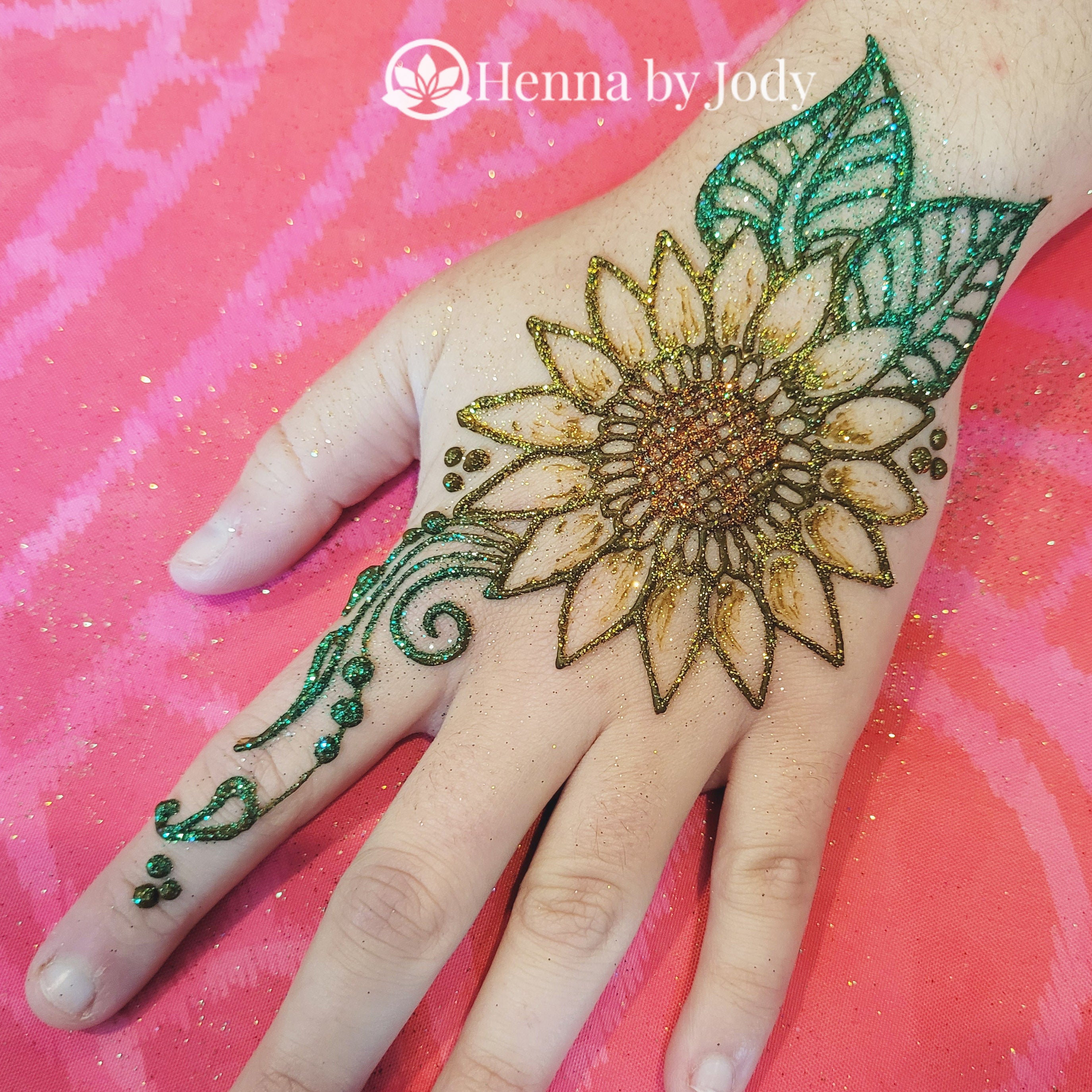 Glitter on a sunflower henna design on a hand. Green leaves, yellow gold petals, and orange center.