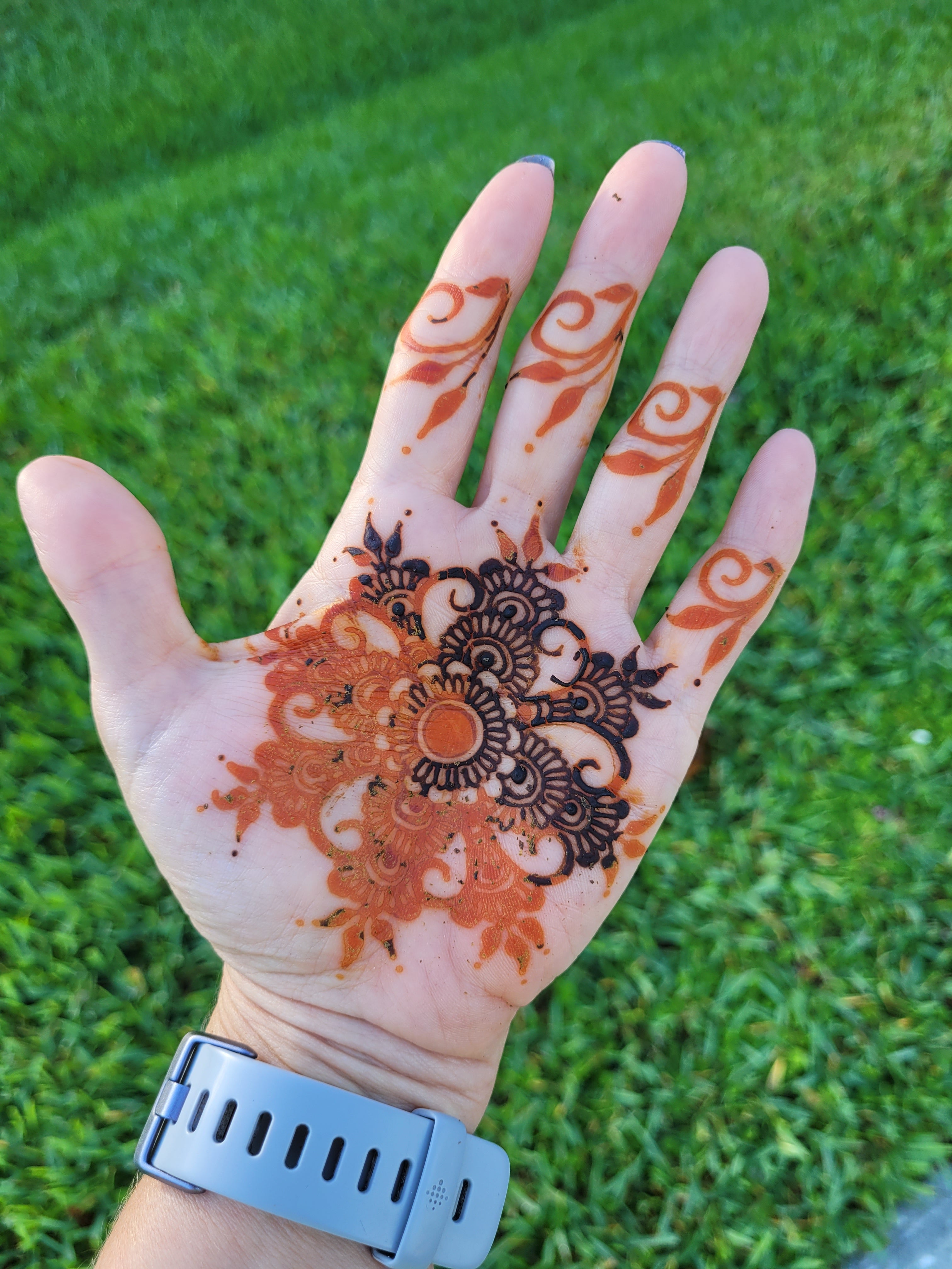 A palm with henna paste and fresh orange henna stain on a grassy background