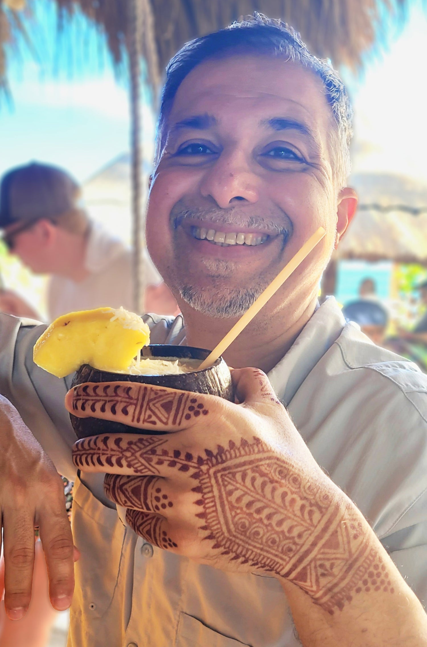 Picture of Asad smiling with a coconut drink with aa beautiful henna design on his hand.