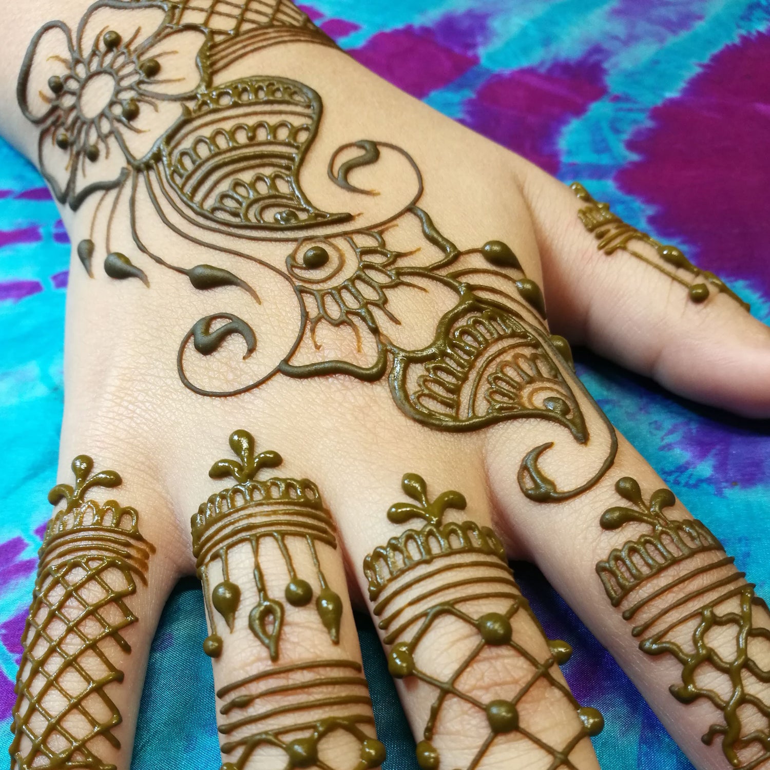 A hand with a classic Indo-Arabic henna design with wet henna paste