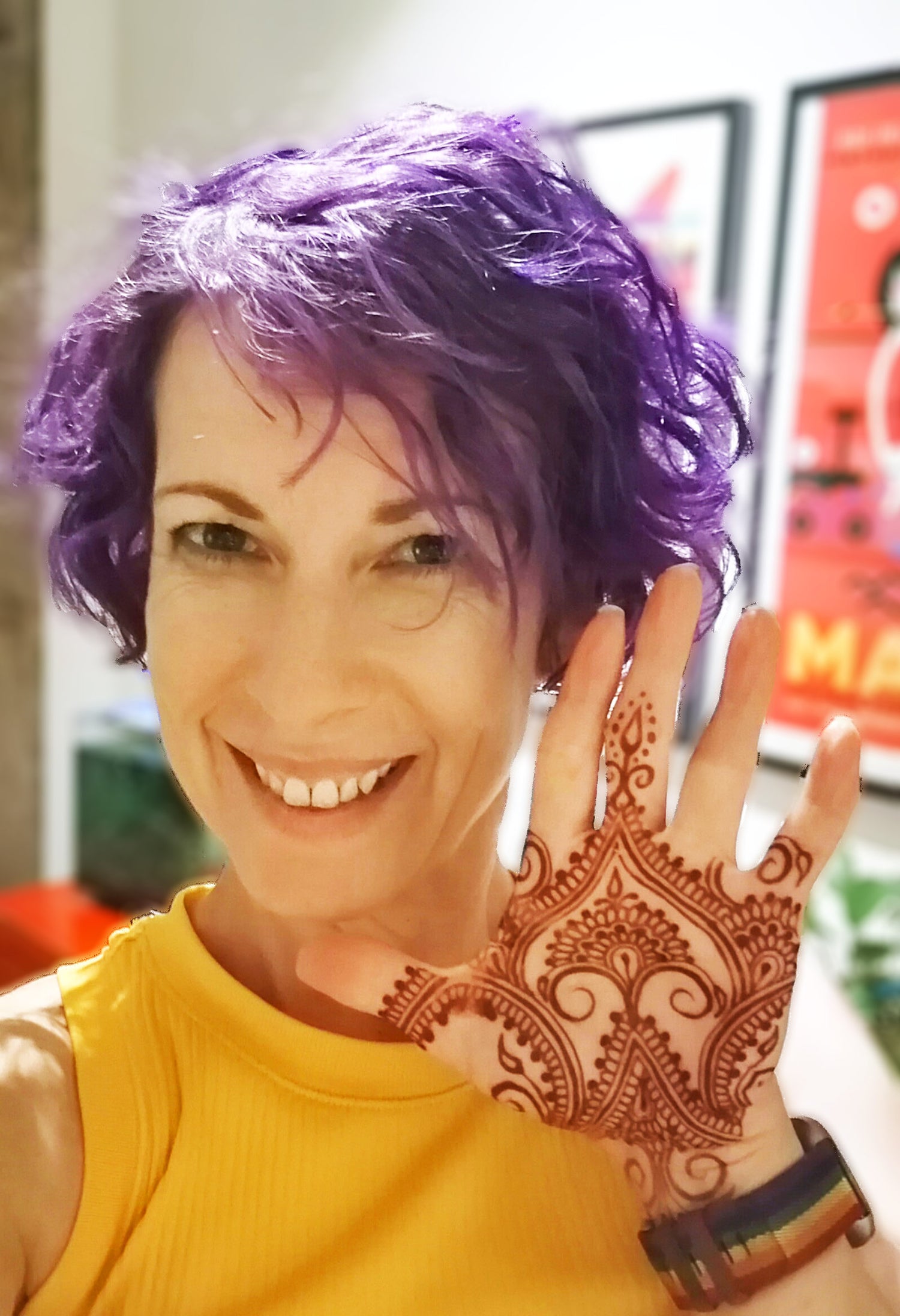 Picture of Jody smiling and holding up her palm beside her face to show off an Indian style henna design.