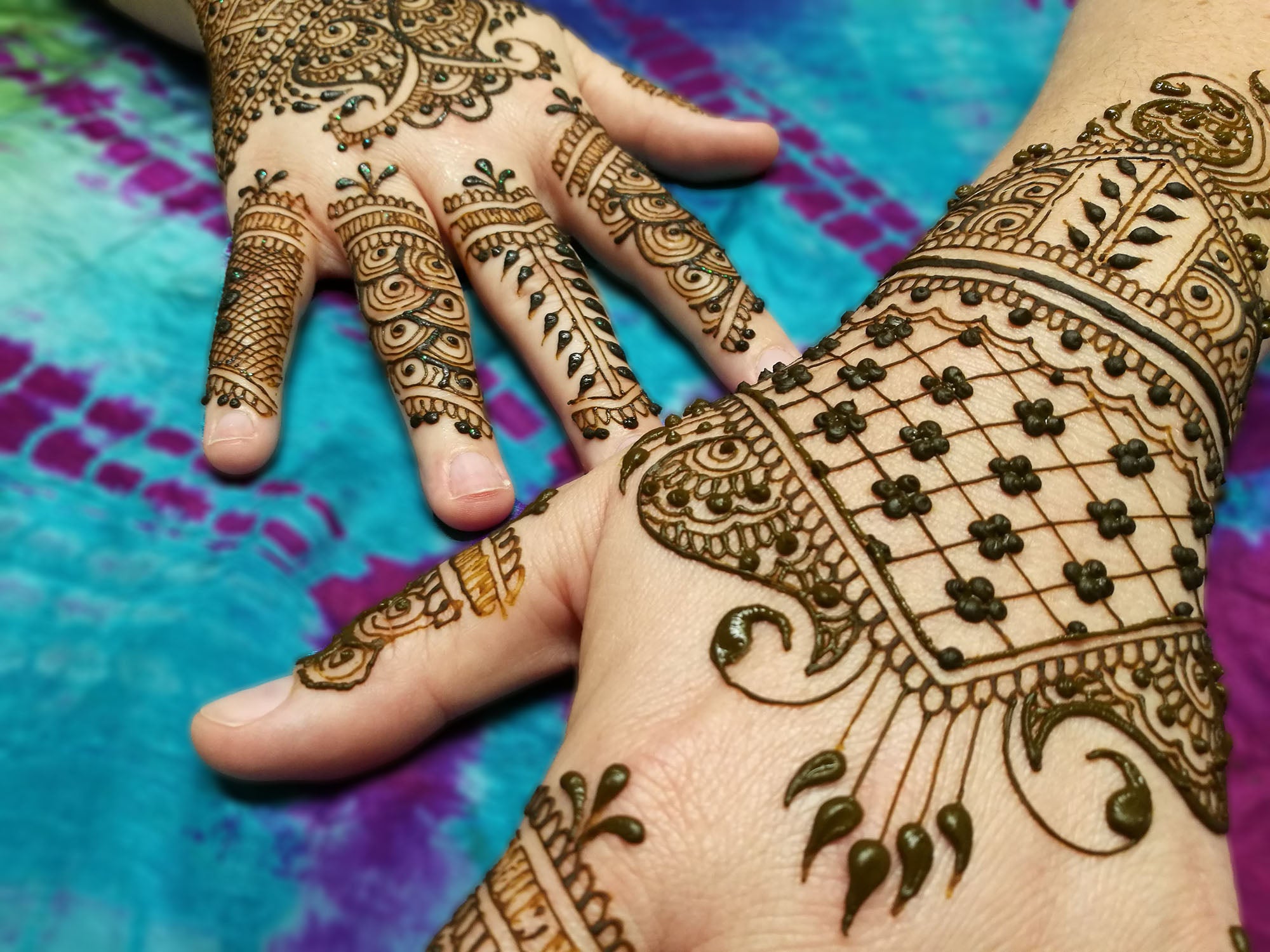 Two offset hands with classic Indian style henna design on them. Henna paste still on the skin