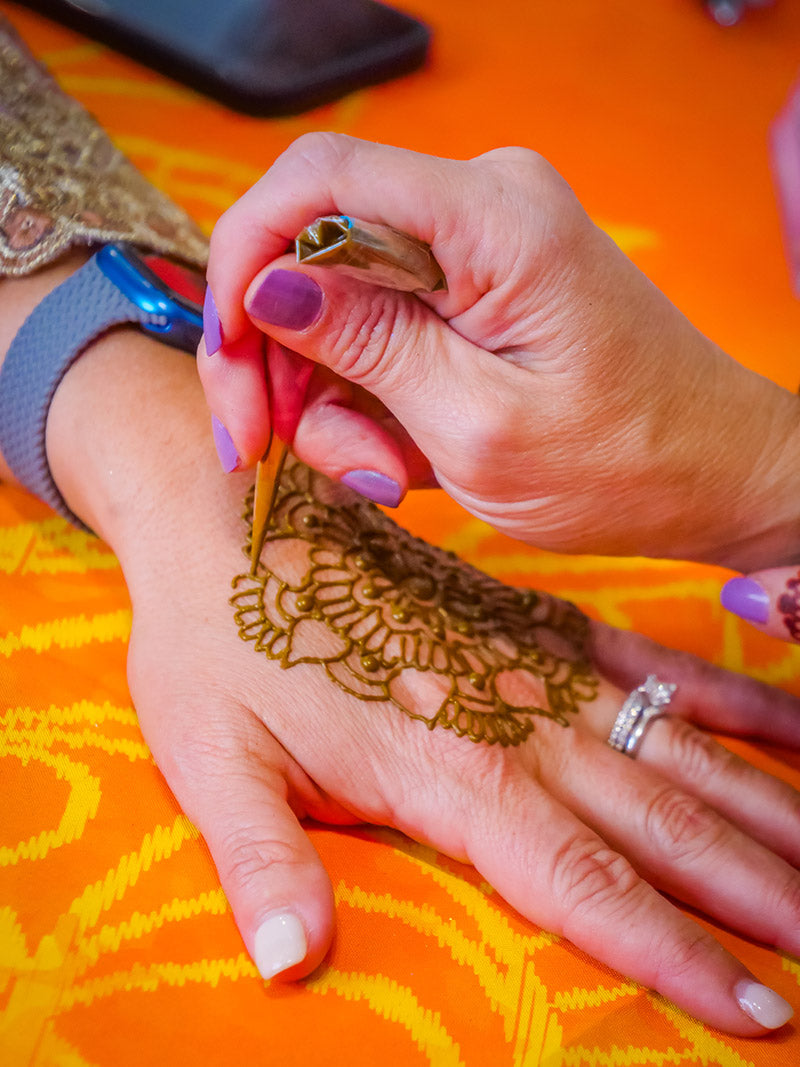 A hand using a henna cone to apply a mandala henna design on top of another hand