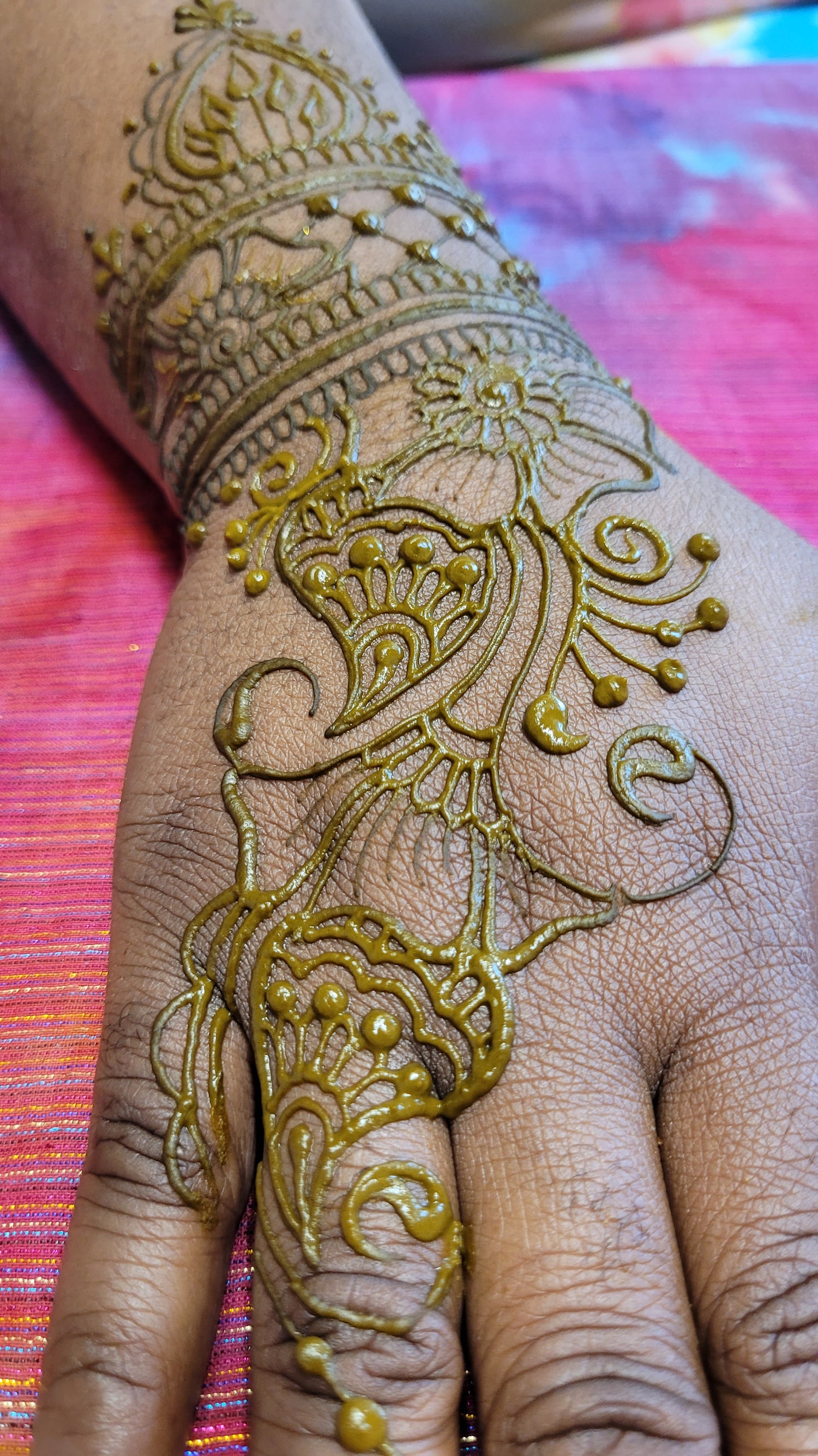 Henna paste in a sangeet strip henna design on top of a hand with brown skin