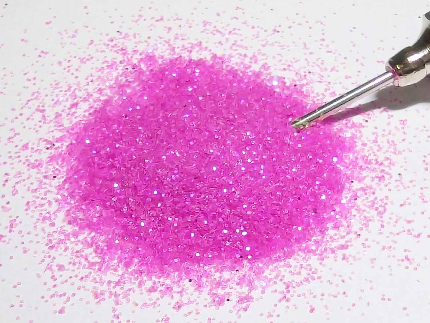 Small pile of UV cosmic berry pink body glitter with applicator tip in the glitter