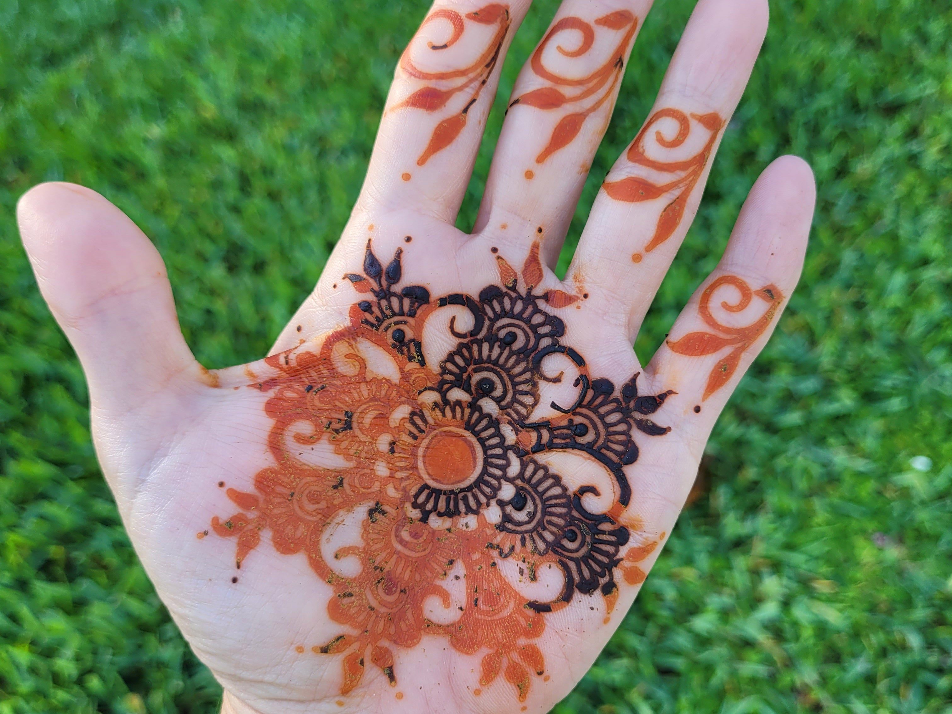 Mandala design on teh palm with half the paste scrapped away and a bright orange stain